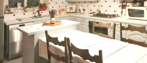 A kitchen with white cabinets, a stainless steel refrigerator, a microwave, and a dining area with a table and chairs.