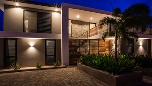 Una casa moderna de dos pisos con un camino de ladrillo, barandal de madera y una escalera que lleva a un nivel superior.