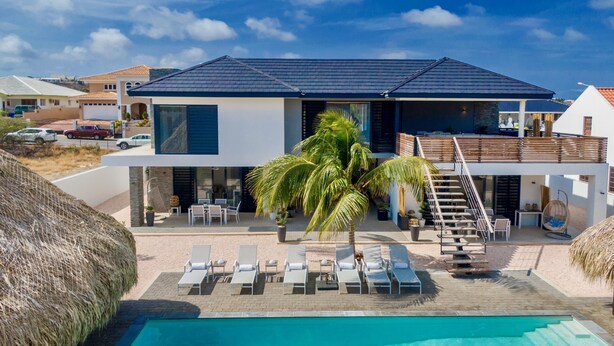 Una casa moderna de dos pisos con piscina, sillas de descanso y una escalera que conduce a una terraza.