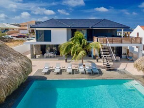 Una casa moderna de dos pisos con piscina, sillas de descanso y una escalera que conduce a una terraza.