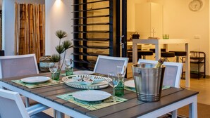 Un comedor con una mesa lista para dos, una pared decorativa de bambú y una cocina moderna al fondo.