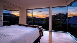 Una camera da letto con un letto grande, vista sul tramonto e un balcone con porte in vetro.