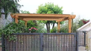 Eine hölzerne Pergola über einem Bambuszaun, mit einem Garten im Hintergrund.