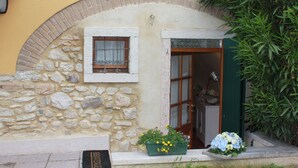 Eine Steinfassade mit einem kleinen Fenster und einer Tür, ein Blumentopf mit gelben Blüten und eine grüne Tür.