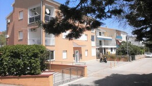 Un edificio residenziale a più piani con balconi, un ingresso chiuso da cancello e cielo sereno.