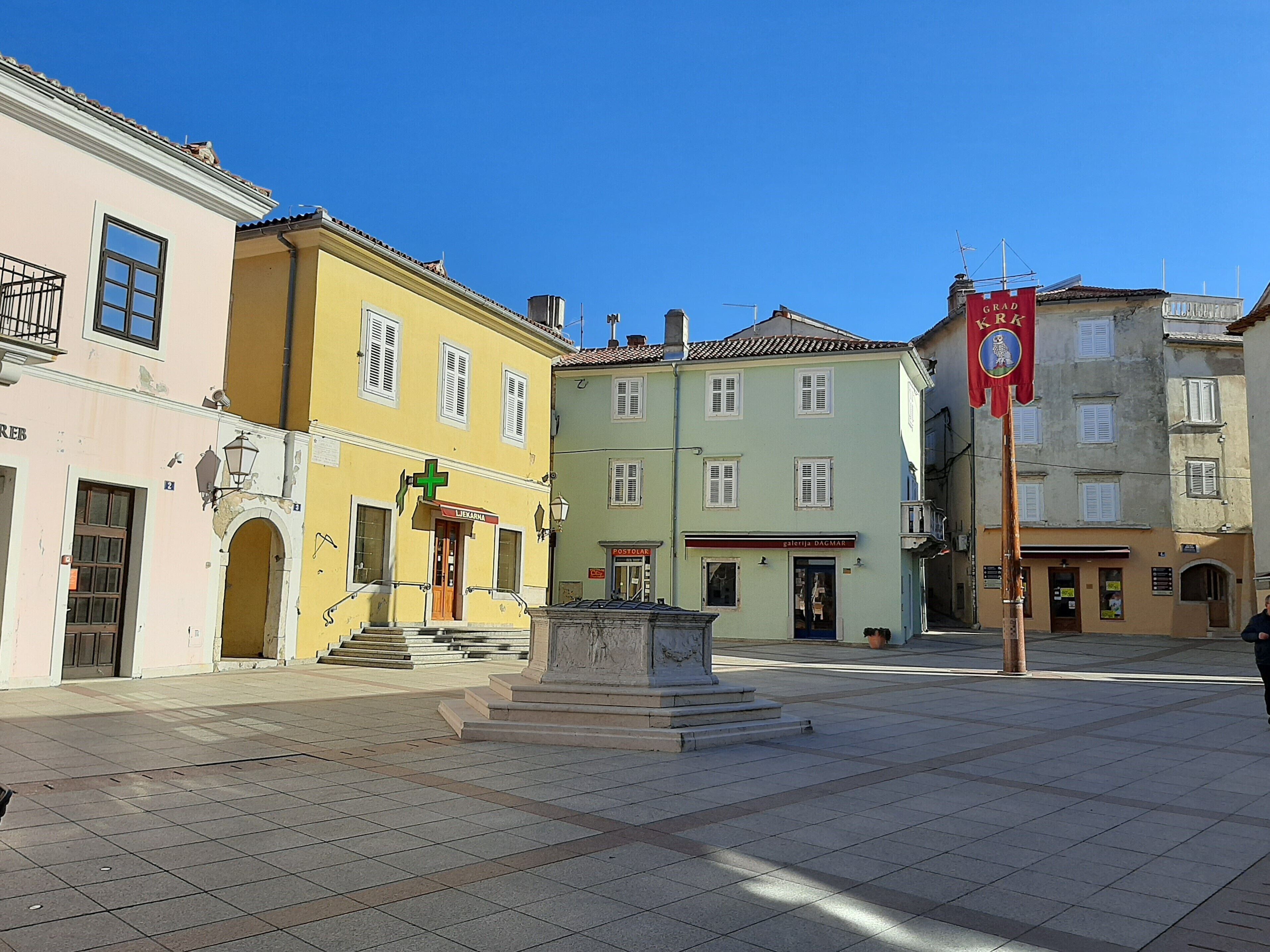 A square with a central monument, buildings with signage, and a clear blue sky.