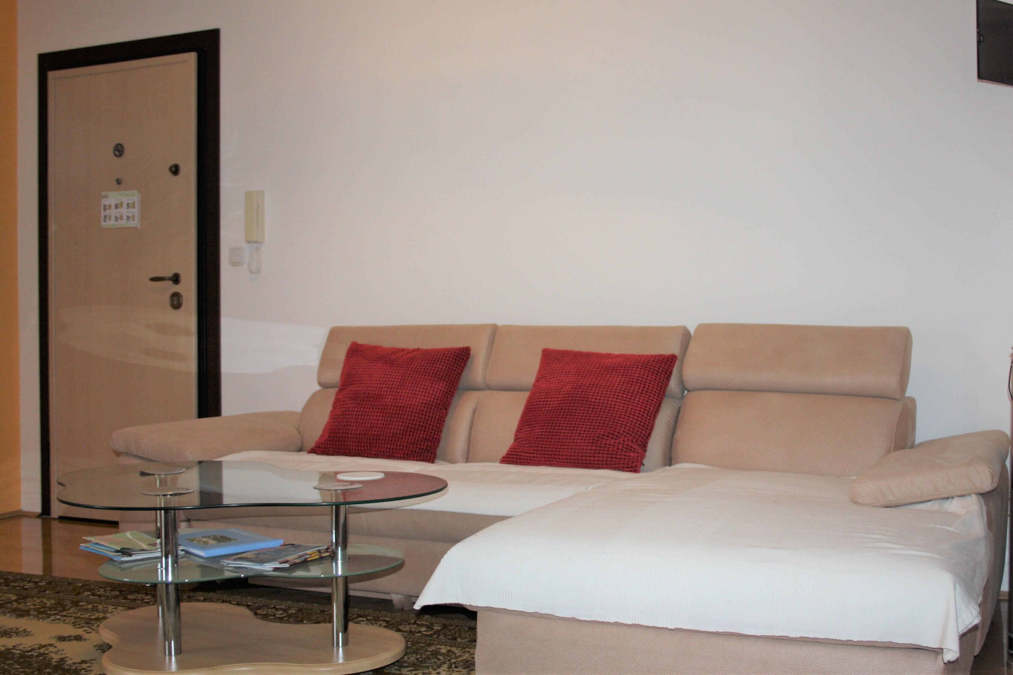 Una habitación de hotel con un sofá color beige, una mesa de centro de vidrio y una cama con ropa de cama blanca.