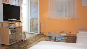 Una camera d'albergo con un letto, un tavolino, una TV su un mobile e una porta che dà su un balcone.