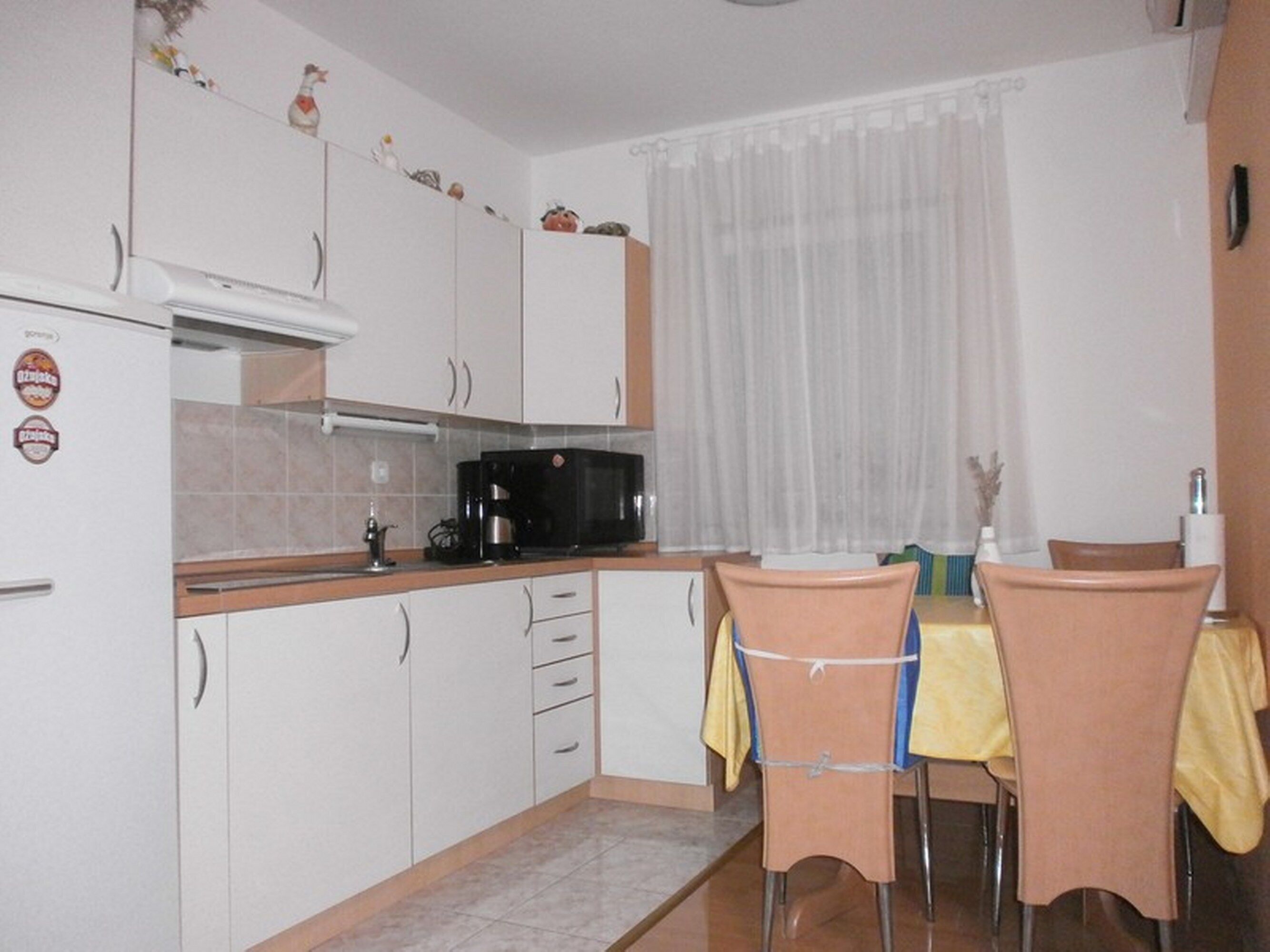 Cozinha compacta com armários brancos, micro-ondas preto e mesa de jantar com cadeiras.