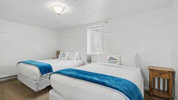 A hotel room with two beds, a small wooden nightstand, a window with blinds, and a ceiling light.