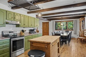A kitchen with green cabinets, a wooden island, stainless steel appliances, and a dining area with a table and chairs. - Huge 3-bedroom home just 1 minute from Yellowstone. Legacy West (West Yellowstone)