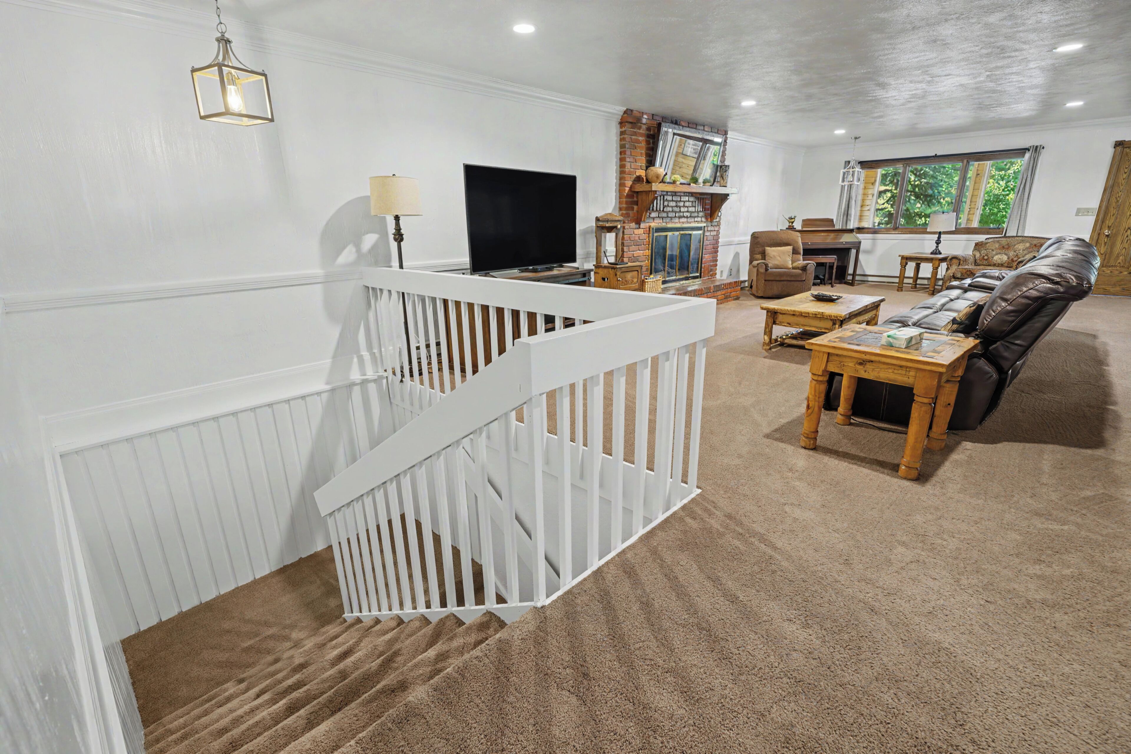 Een woonkamer met een witte balustrade, een open haard, een televisie en een leren bank.