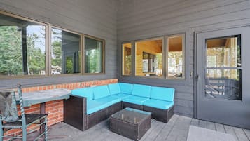 An outdoor patio area with a blue sectional sofa, a glass-top coffee table, and a brick accent wall.