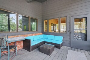 An outdoor patio area with a blue sectional sofa, a glass-top coffee table, and a brick accent wall. - Huge 3-bedroom home just 1 minute from Yellowstone. Legacy West (West Yellowstone)