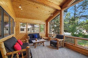 A wooden interior with a sofa, chairs, and a table, large windows, and a view of trees and a vehicle outside. - Huge 3-bedroom home just 1 minute from Yellowstone. Legacy West (West Yellowstone)