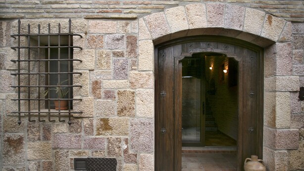 Un bâtiment en pierre avec une porte en bois, une fenêtre grillagée et une petite marche menant à l’entrée.