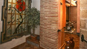 Une pièce avec un mur en briques, une plante en pot, un miroir décoratif et un téléphone d’époque.