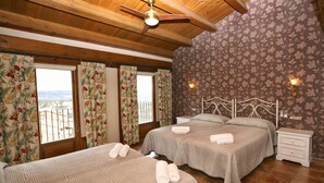 Une chambre avec deux lits, des rideaux à motifs floraux, un plafond en bois et une table de chevet avec une lampe.
