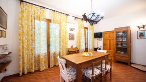 Ein Essbereich mit einem Holztisch, Stühlen, gelben floralen Vorhängen, einer Kristallleuchtre und einem Holzschrank mit Glastüren.