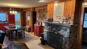 Ein gemütliches Blockhaus mit Kamin aus Naturstein, Holzwänden, einem Essbereich und einer Küche mit roten Schränken.