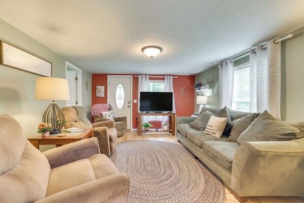 A living room with a sofa, armchairs, a TV, and a coffee table. - Visit Fife Lake & Traverse Bay! Farmhouse Hideaway (Fife Lake)