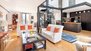 Un salon moderne avec un canapé blanc, une table basse en verre et un escalier menant à l’étage supérieur.