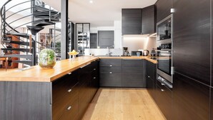 Une cuisine moderne avec un escalier en colimaçon, des meubles de couleur sombre et des appareils électroménagers en acier inoxydable.