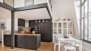Une cuisine moderne dotée d’un îlot central, d’un coin repas avec une table et des chaises blanches, et d’un meuble blanc aux portes en verre.