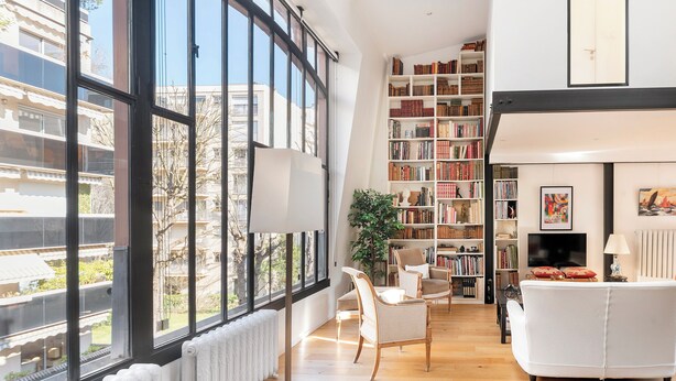 Un salon moderne avec une grande fenêtre, une bibliothèque, un canapé et un téléviseur.