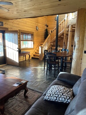 A wooden interior with a staircase, a dining area, and a seating area with a sofa and a table.