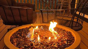 A circular outdoor fire feature with flames, surrounded by outdoor furniture on a wooden deck.