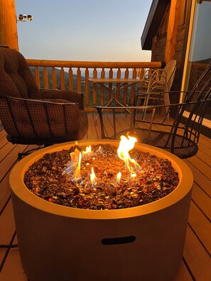 A circular outdoor fire feature with flames, surrounded by outdoor furniture on a wooden deck.