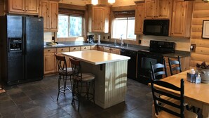 Una cocina amplia con armarios de madera, un refrigerador negro, un microondas y una isla grande con taburetes de bar.