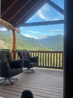 A wooden deck with two upholstered chairs facing a mountainous landscape.
