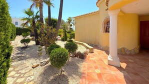 Un patio con un sendero adoquinado, palmeras y un edificio de fachada amarilla y columnas blancas.