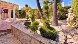 Un jardín ajardinado con palmeras, una estatua y un edificio con tejado de baldosas.