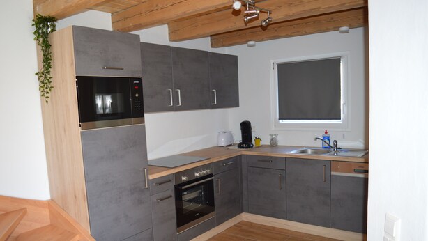 Una cocina moderna con armarios grises, horno empotrado, microondas y encimera de madera.