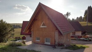 Una casa de madera con techo rojo, entrada pavimentada y un pequeño jardín.