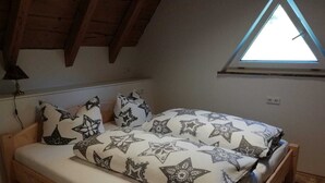 Un dormitorio pequeño y acogedor con techo inclinado, estructura de cama de madera y tragaluz.