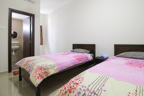 Two single beds with pink and white bedspreads, a nightstand, and a door leading to a bathroom with a sink and mirror.