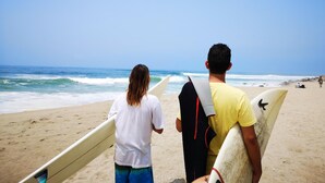 Two individuals with surfboards on a beach. - Surfari Punta Rocas (Punta Negra)
