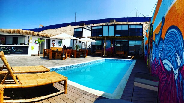 A pool area with lounge chairs, umbrellas, and a mural. - Surfari Punta Rocas (Punta Negra)