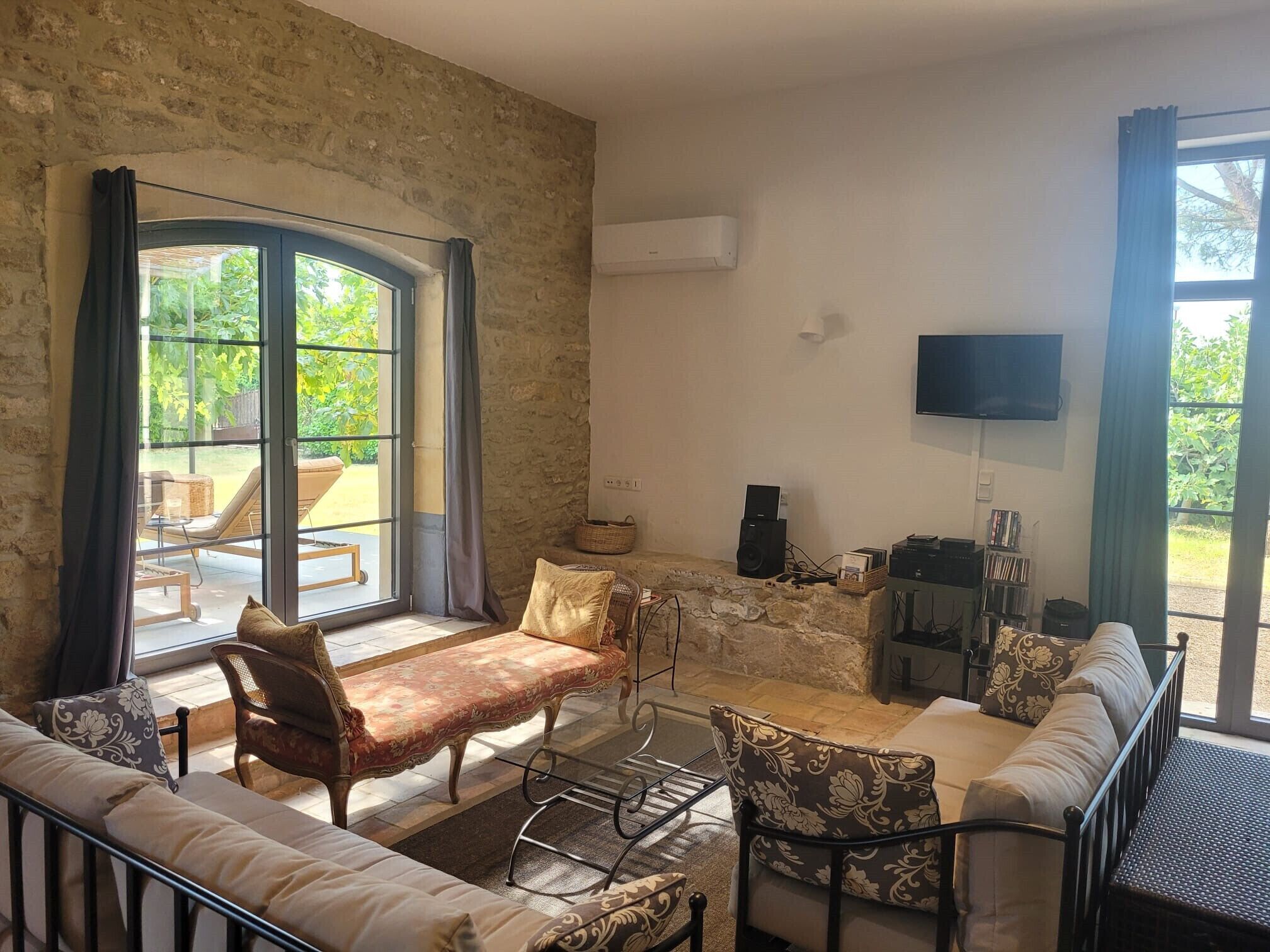 A furnished living room with a stone wall, a large window, a flat-screen TV, and a fireplace.