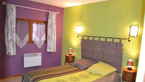Un dormitorio con cama, dos mesitas de noche con lámparas, una ventana con cortinas y un calentador fijado a la pared.