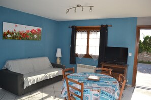 Een kamer met een blauwe wand, een bank, een tafel met stoelen, een televisie en een schilderij van bloemen.