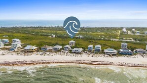 Eine Luftaufnahme einer Küstenwohngegend mit Immobilien direkt am Strand, darunter Häuser mit mehreren Stockwerken und großen Fenstern, vermutlich mit Meerblick.