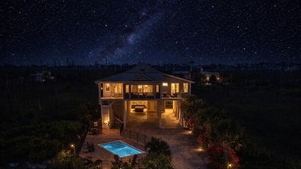 Ein zweistöckiges Haus mit Pool, umgeben von Vegetation, unter einem sternenübersäten Nachthimmel.