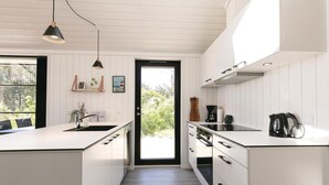 A modern kitchen with white cabinetry, a central island, a black kettle, and a window with a view of greenery.