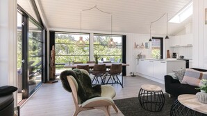 A modern kitchen with white cabinets, a dining area with a table and chairs, and a large window with a view of greenery.