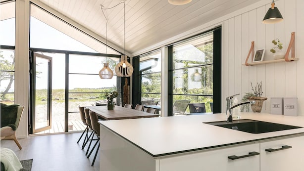 A modern kitchen with large windows, a central island, and a dining area with chairs.